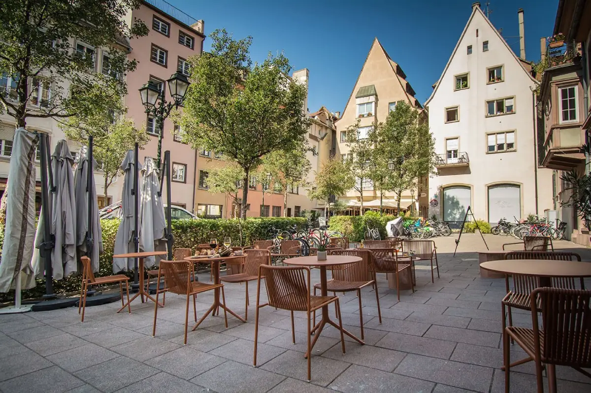 Espace extérieur de l’Hôtel Rohan Strasbourg avec tables, chaises et arbres en arrière-plan