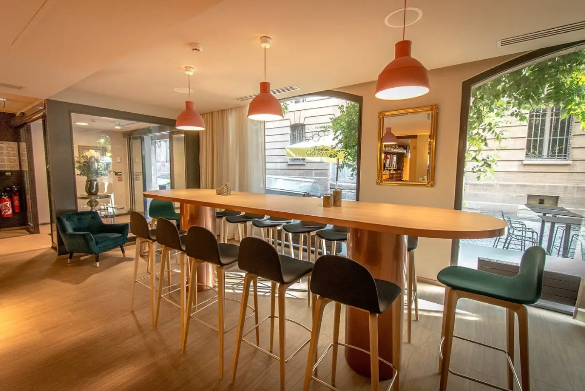 Espace intérieur de l’Hôtel Rohan Strasbourg avec table haute, chaises hautes et luminaires suspendus