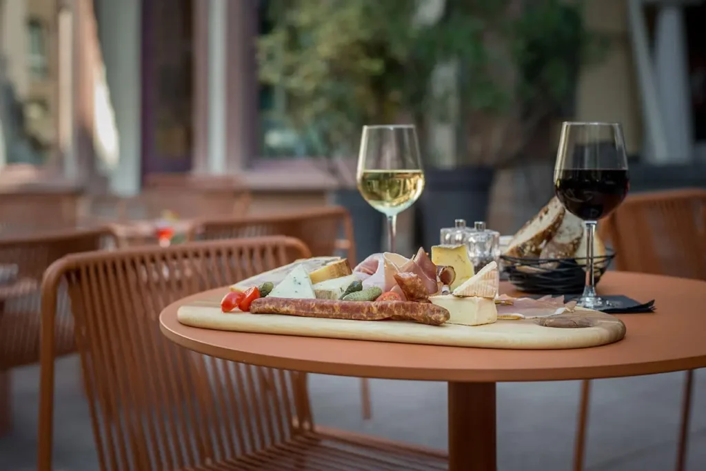 Service Bar de l’Hôtel Rohan Strasbourg avec planche de fromages et charcuterie, verres de vin et table en terrasse