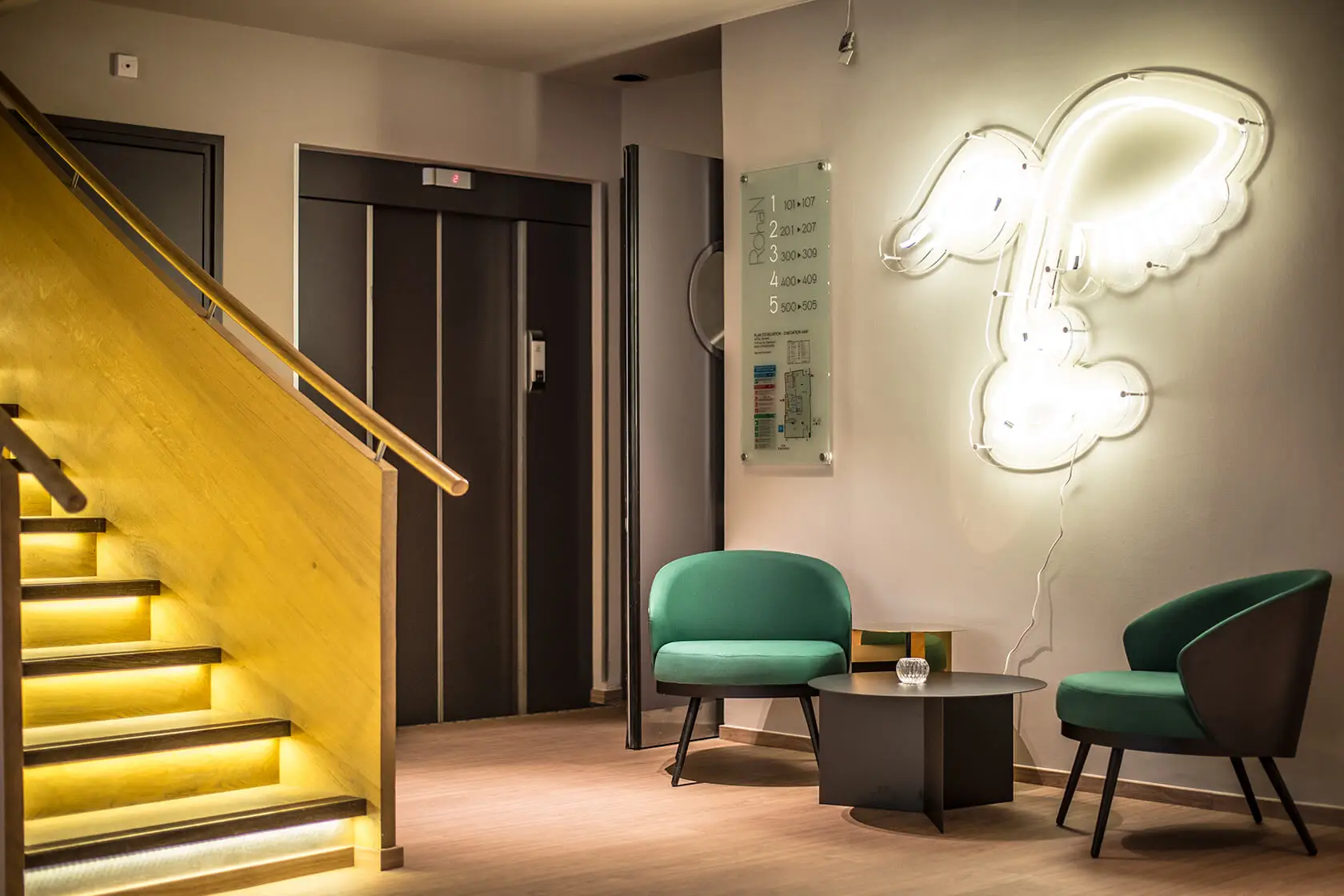 Bereich des Service Nützliche Informationen im Hotel Rohan Straßburg mit beleuchteter Treppe, grünen Sesseln und dekorativer Wandbeleuchtung